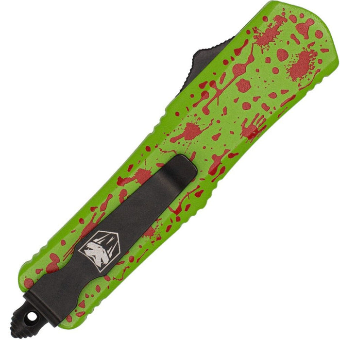 A tactical utility knife with a bright lime green handle featuring a red blood splatter pattern, a black clip, and a black textured guard, shown on a plain white background.